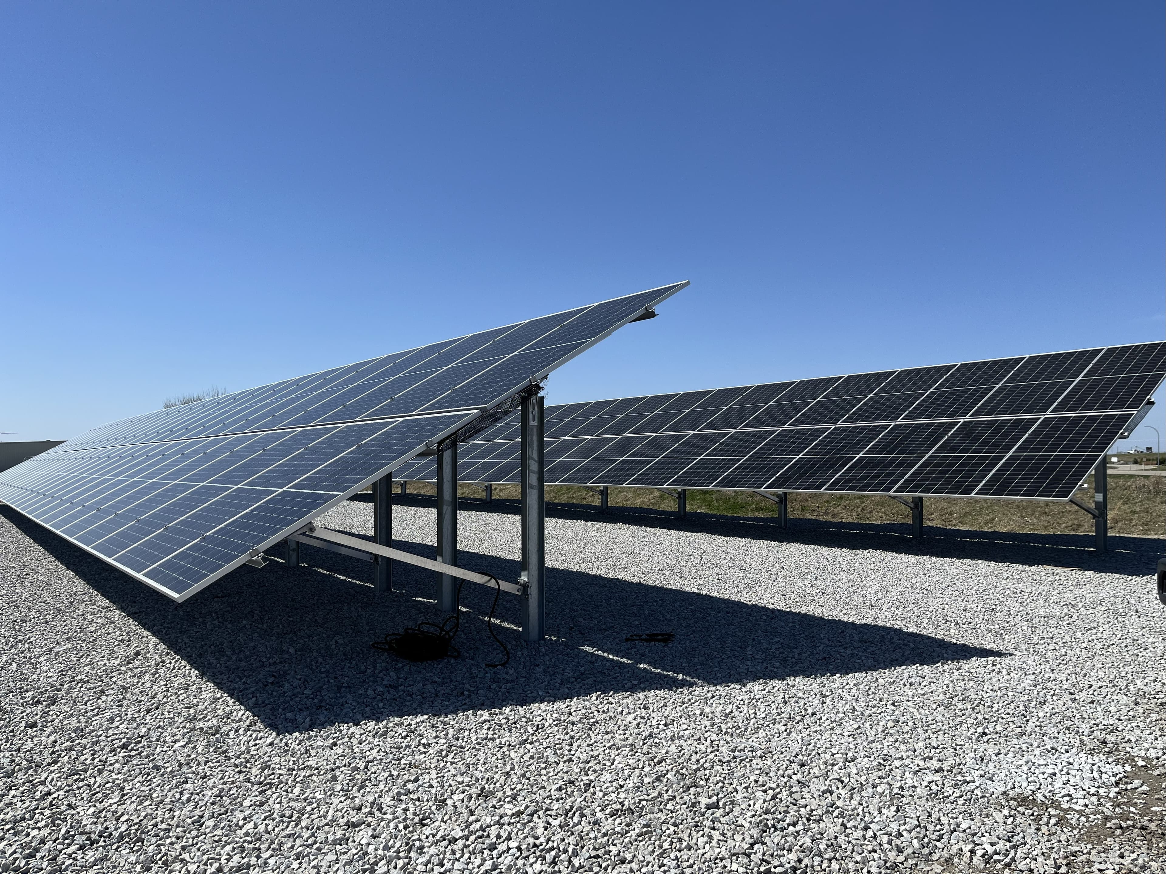 Ground-mounted solar array on open grassland, afternoon light, dramatic sky