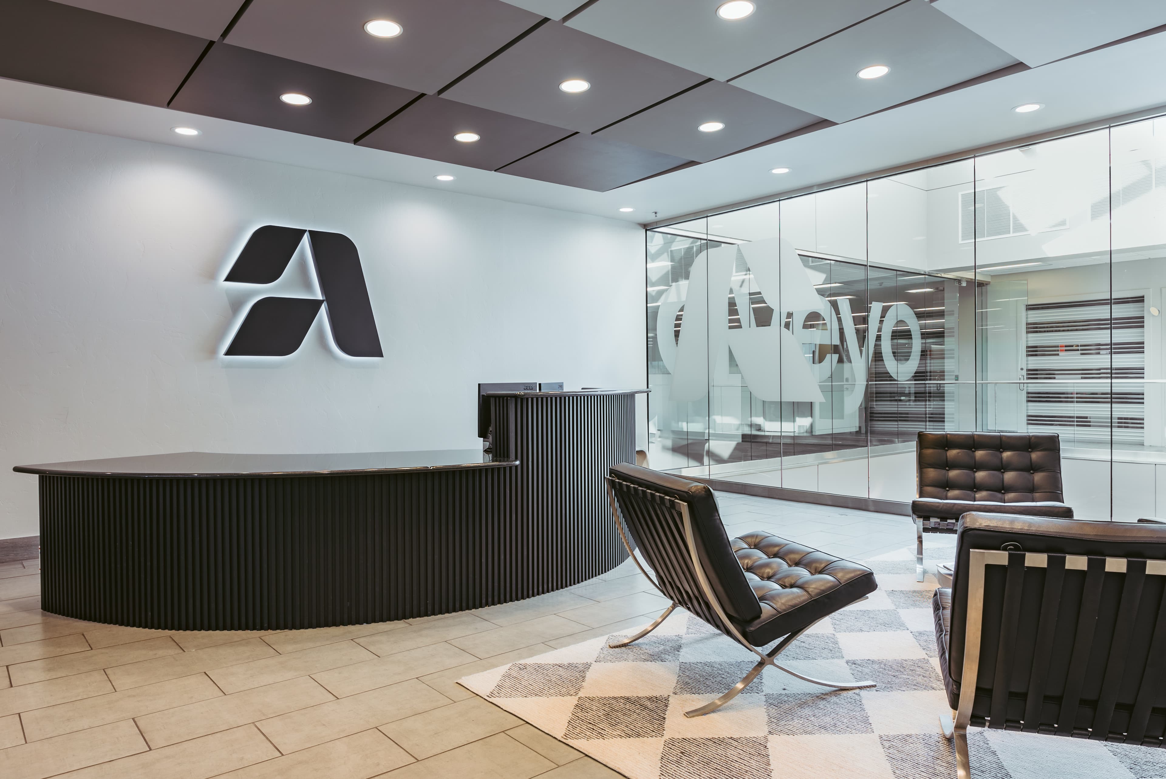 Aveyo office lobby with illuminated brand logo, Barcelona chairs, and glass walls
