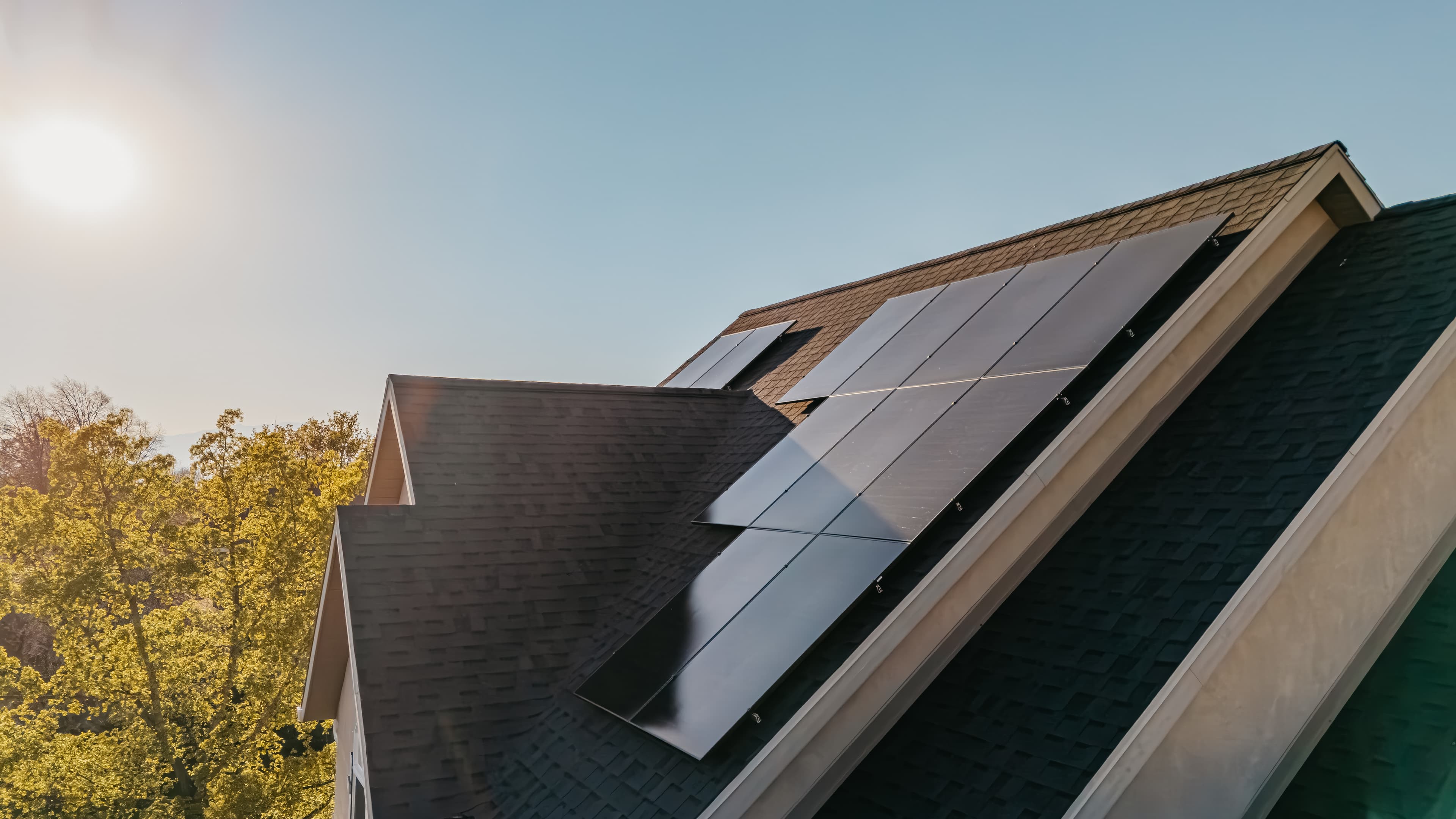Black rooftop solar panels installed on a sloped house roof in warm sunlight