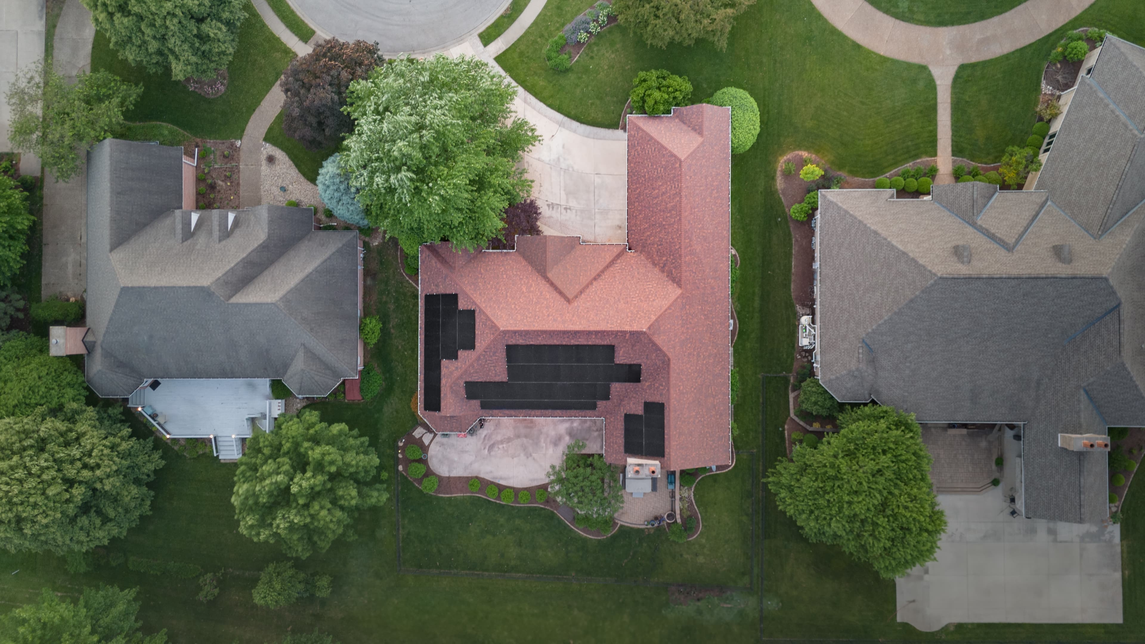 Modern home with dark solar panels on roof, golden hour, lush landscaping